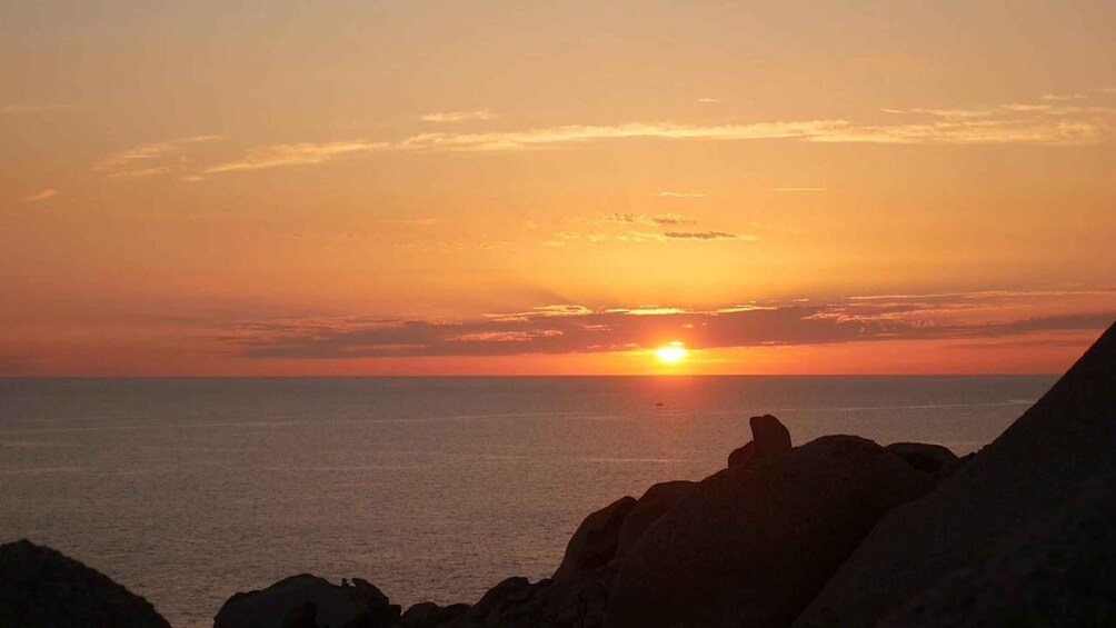 A sunset over the ocean with rocky formations in the foreground. 1