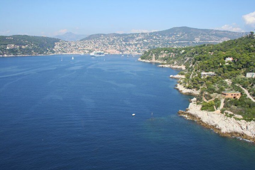 A coastal city with a clear blue sea, a rocky shoreline, and distant hills. 2