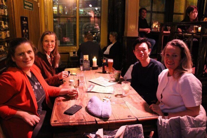 A group of people seated around a wooden table in a dimly lit indoor setting. 4