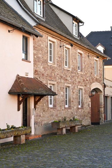 A stone building with a tiled roof, a wooden bench, and a cobblestone street. 1