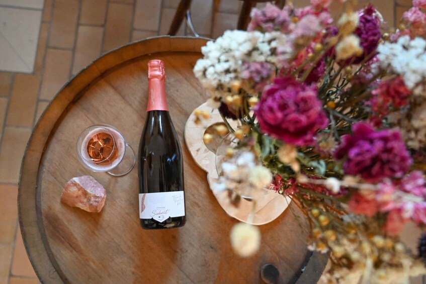 A bottle of wine on a wooden barrel, a glass of wine, and a bouquet of flowers. 3
