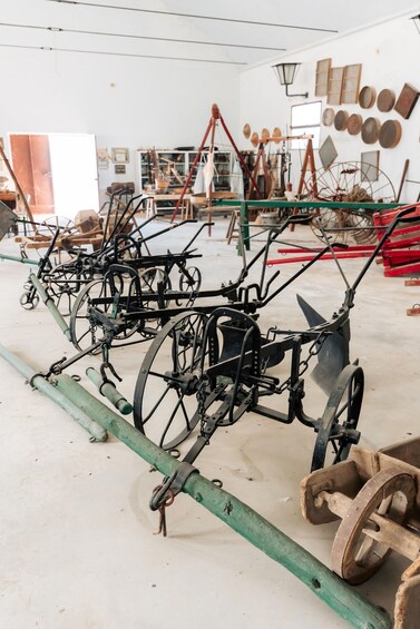 A workshop with antique farming equipment, including plows and wheelbarrows. 3