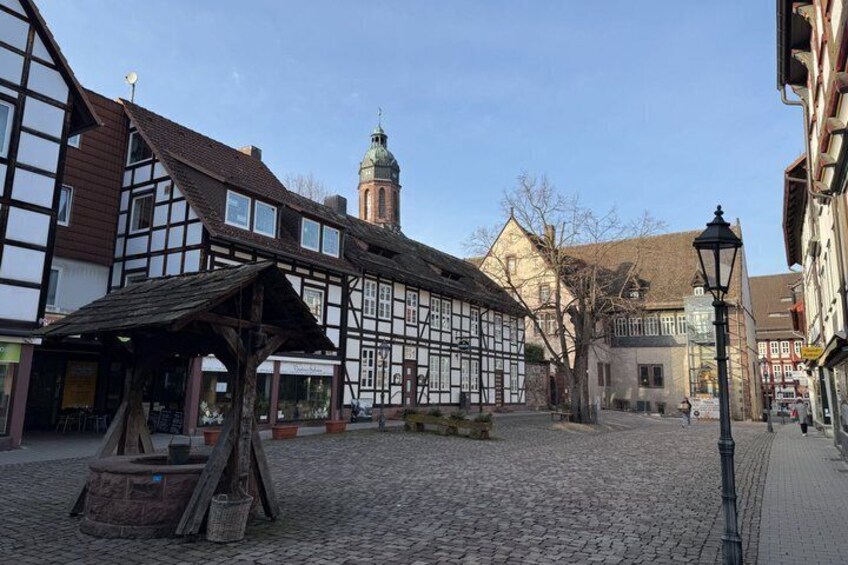 A cobblestone street with half-timbered buildings, a church tower, and a street lamp. 1
