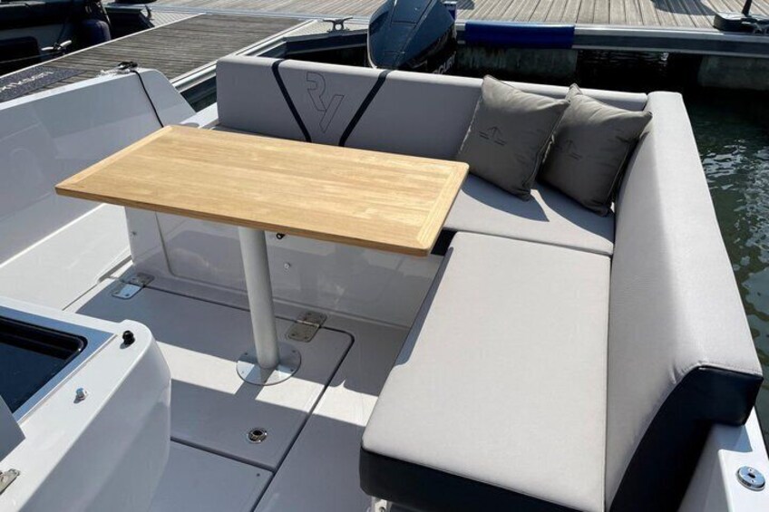 A boat's deck with a wooden table, cushioned seating, and a logo on the backrest. 2