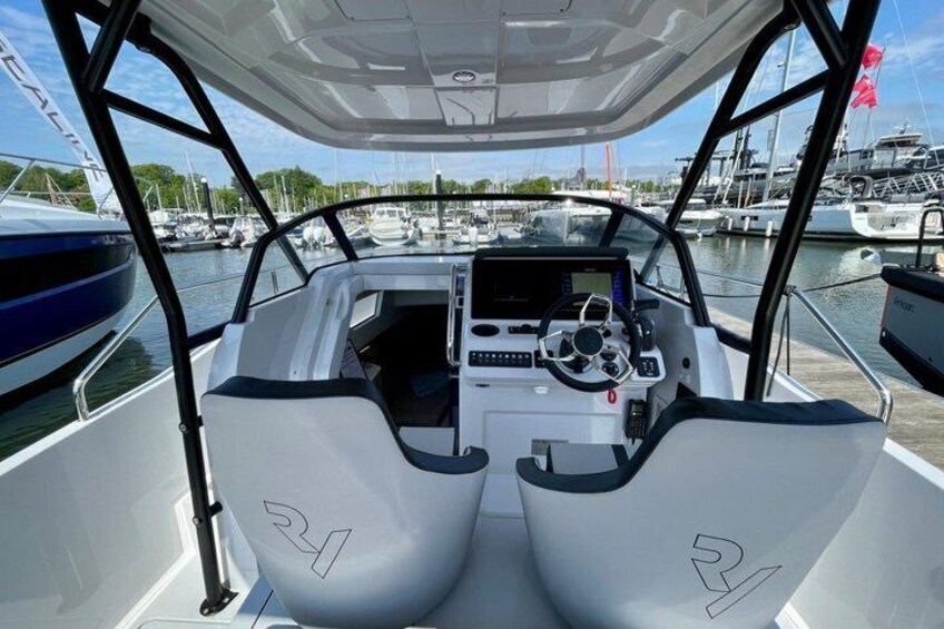 A boat's cockpit with a steering wheel, control panel, and two seats marked '24'. 3