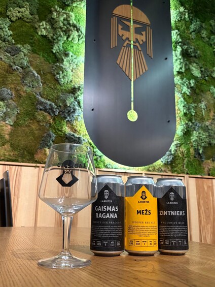 A glass, three beer cans, and a wall with a logo. 2