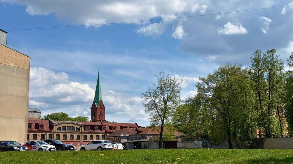 A church with a green spire, parked cars, and a grassy field. 5