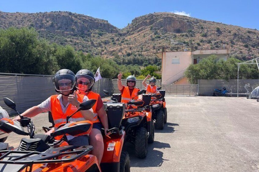 Three people on quad bikes in a parking lot with mountains in the background. 3
