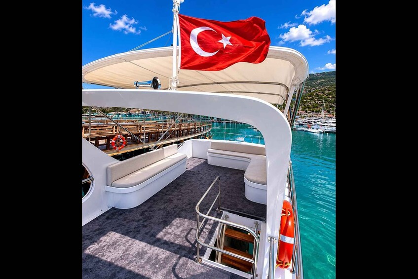 A boat deck with a Turkish flag, a lifebuoy, and a view of a marina with boats and a mountainous landscape. 2