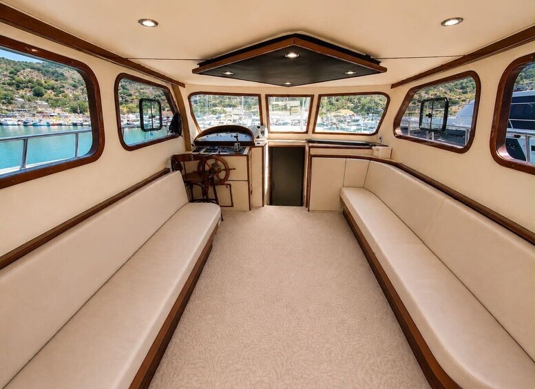 A boat interior with a central bench, a steering wheel, and windows overlooking a marina. 5