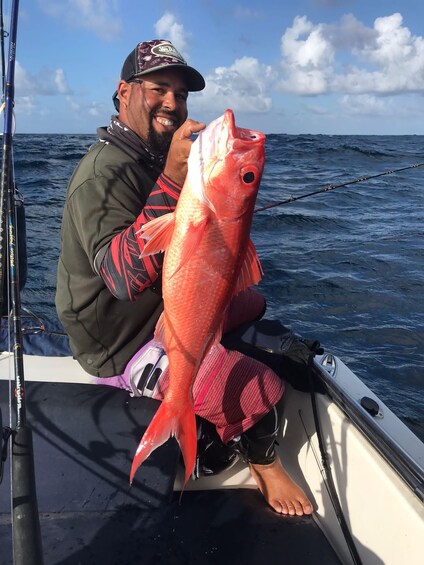 A person holding a large red fish on a boat in the ocean. 3