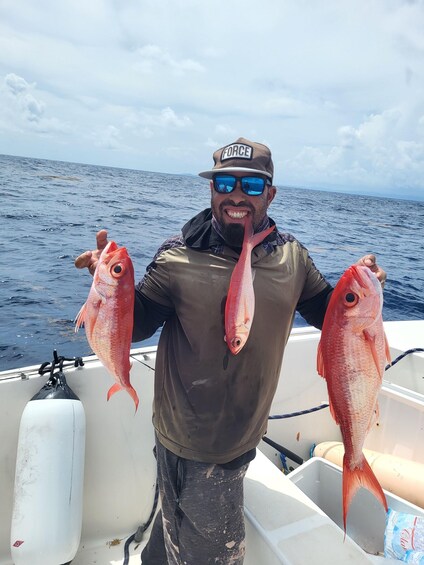 A person holding two red fish on a boat with the ocean in the background. 1