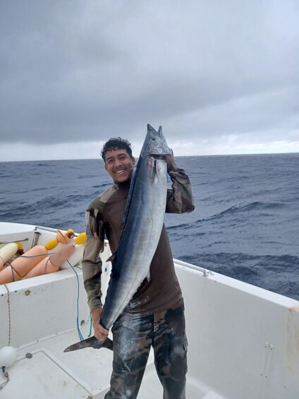 A person holding a large fish on a boat with the ocean in the background. 2