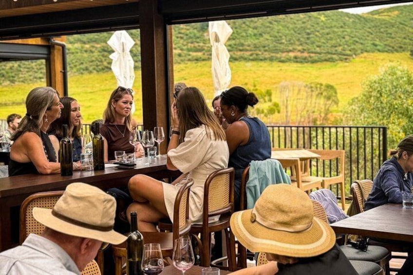 A group of people dining at an outdoor restaurant with a view of a green landscape. 3