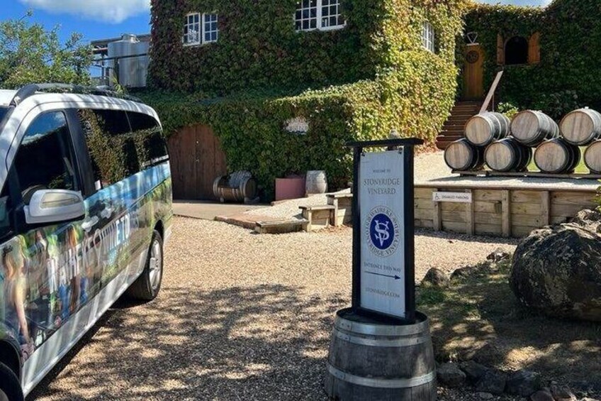 A vintage car parked in front of a vineyard with barrels and a signboard. 5