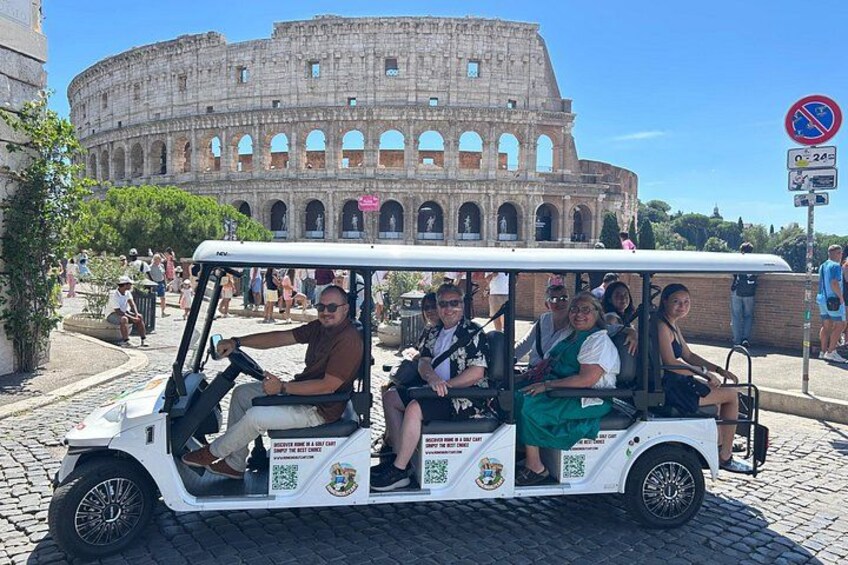 A white tour vehicle with passengers in front of the Colosseum. 5