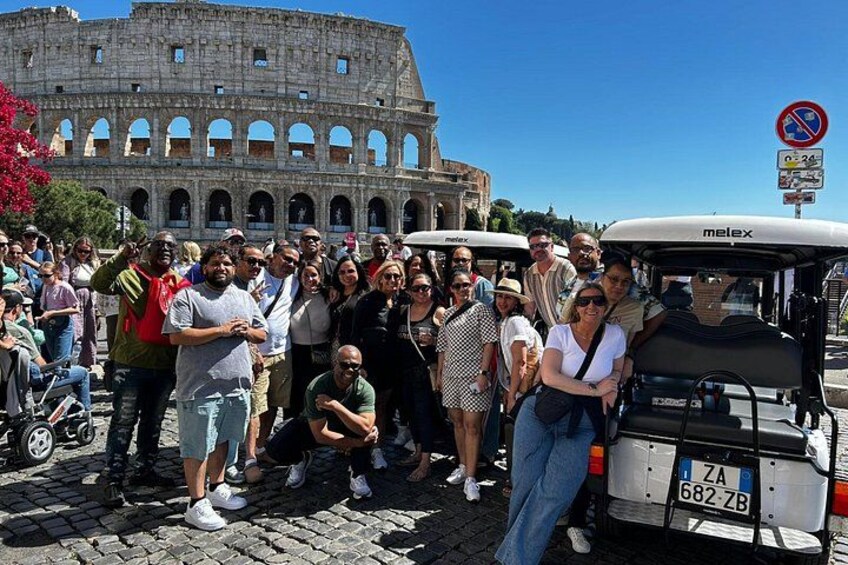A group of people posing in front of the Colosseum with a golf cart in the foreground. 4