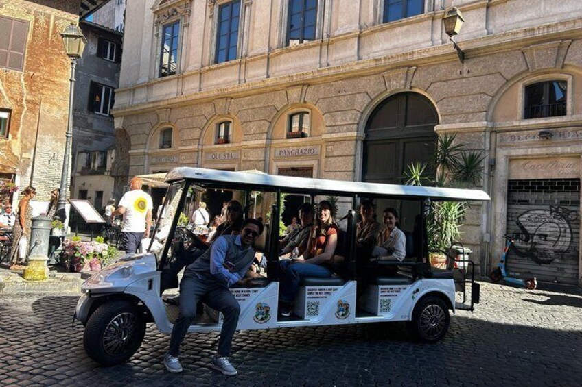 A white tour bus with passengers, parked in front of a historic building with arched windows and a sign reading 'Piazza.' 4