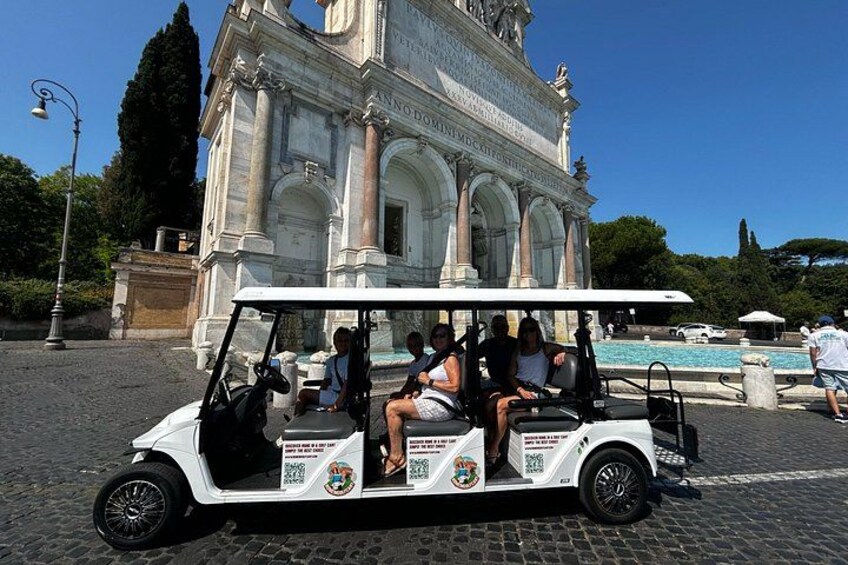 A white golf cart with passengers, parked in front of a large historical monument with columns and inscriptions. 2