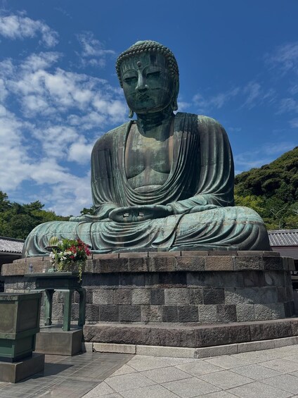 A large seated Buddha statue with a floral arrangement in front. 1