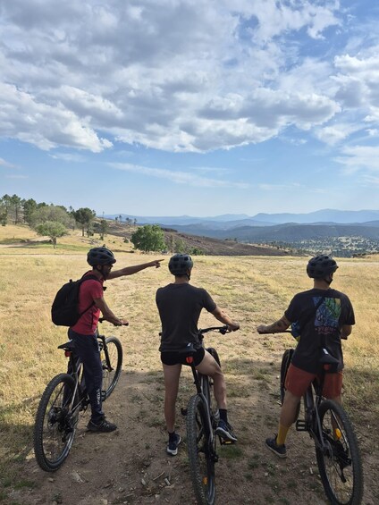 Three cyclists on a dirt path with a view of distant mountains and a town. 4