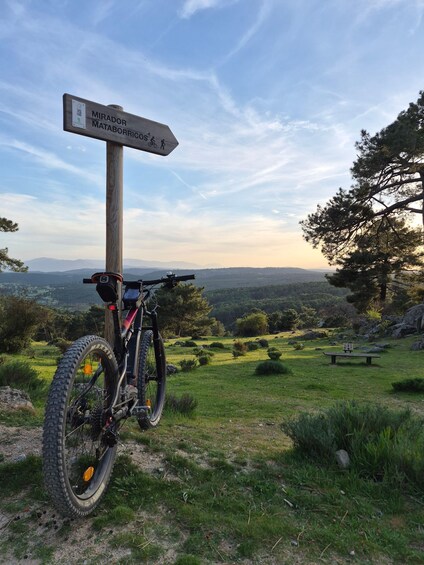 A mountain bike parked next to a wooden signpost with a view of a mountainous landscape. 1