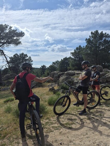 Three people on a mountain biking trail with rocky terrain and pine trees. 3
