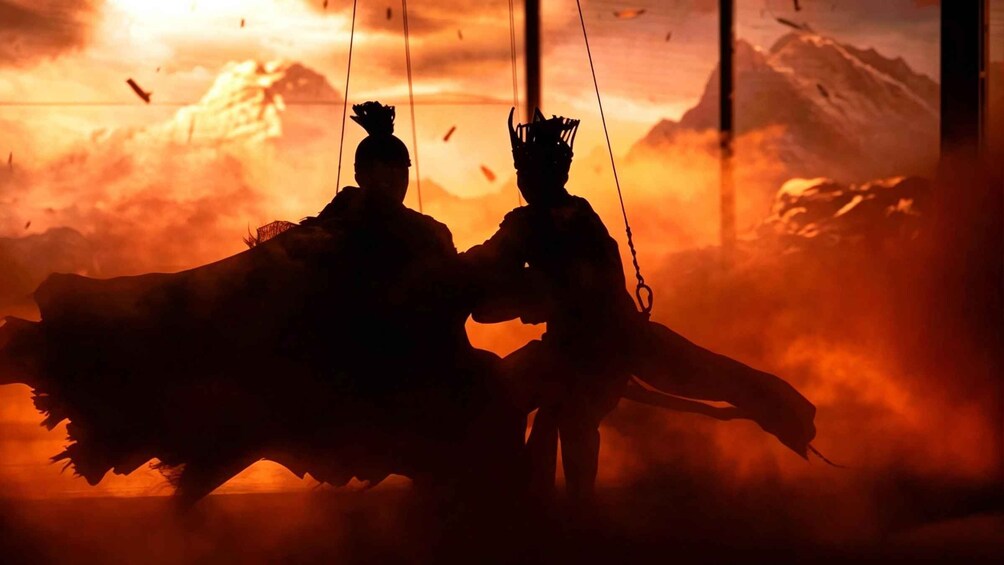 Two figures silhouetted against a fiery sunset with mountains in the background. 3
