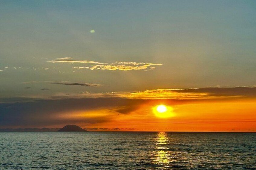 A sunset over a calm sea with a distant island and a clear sky. 4
