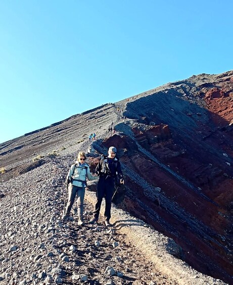 Two people hiking on a rocky trail with a mountainous landscape in the background. 1