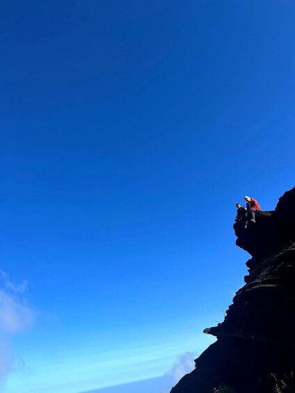 A person sitting on a cliff edge with a clear blue sky in the background. 3