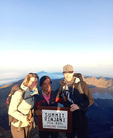 Three people standing on a mountain peak with a sign that reads 'Summit Rinjani 3726 MDPL.' 2