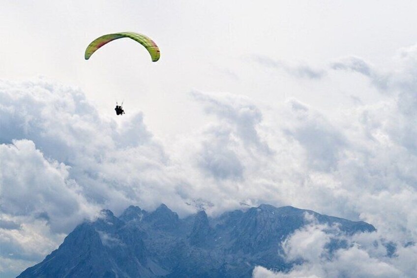 A paraglider flying above a mountain range with clouds. 2