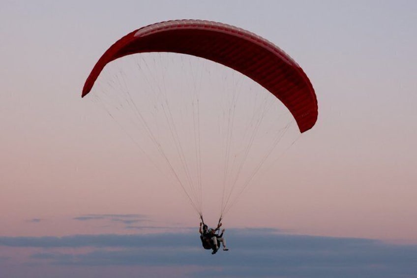 A person paragliding with a red canopy against a twilight sky. 5