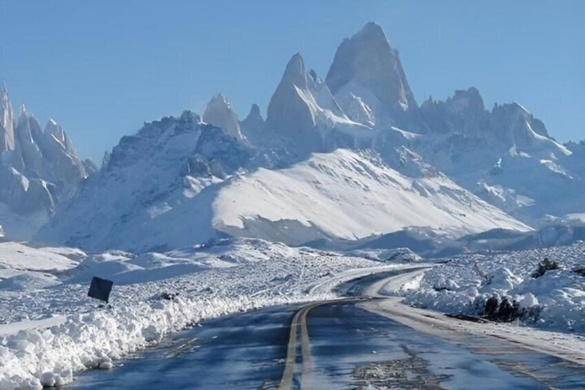 A snow-covered mountain road with a clear sky and sharp peaks in the background. 3