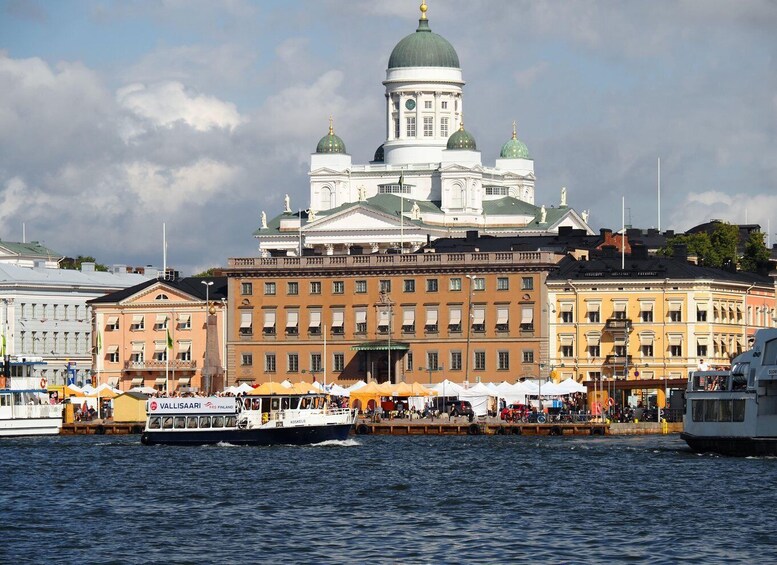 A waterfront with a prominent white building with green domes, a docked ferry, and a crowd of people. 1