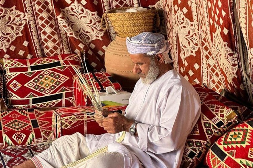 A man sitting on a patterned carpet, holding a traditional woven basket. 5