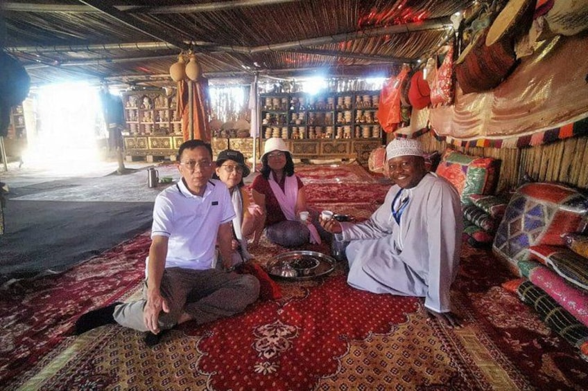 A group of people sitting on a patterned carpet inside a building with shelves of colorful fabrics. 4