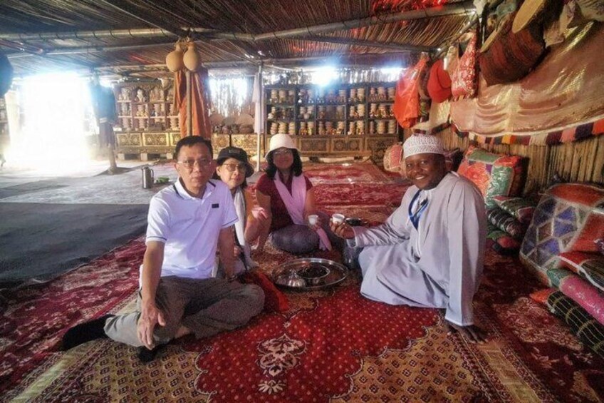 A group of people sitting on a patterned carpet inside a building with shelves of goods in the background. 5
