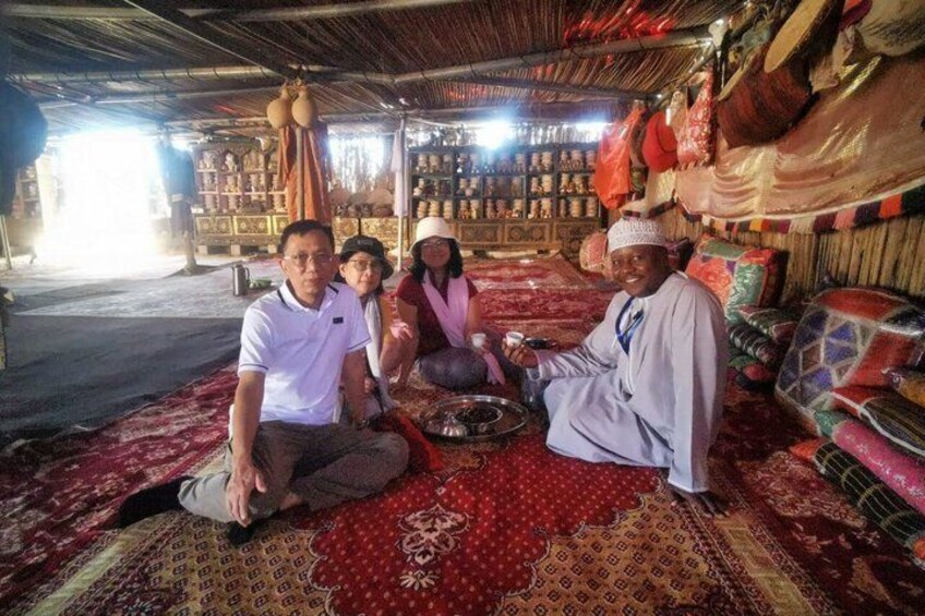 A group of people sitting on a patterned carpet inside a building with shelves of goods in the background. 3