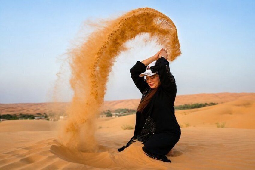 A person in a black outfit with a white cap, standing in a desert with sand being kicked up. 1