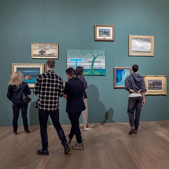 People viewing art in a gallery with wooden floors and teal walls. 2