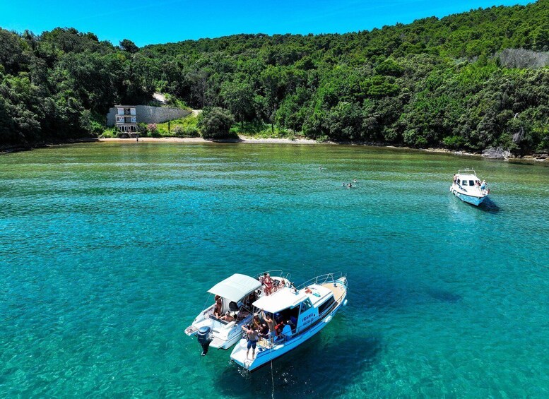 A boat named 'IRENA' anchored in clear turquoise waters, surrounded by lush green hills. 1