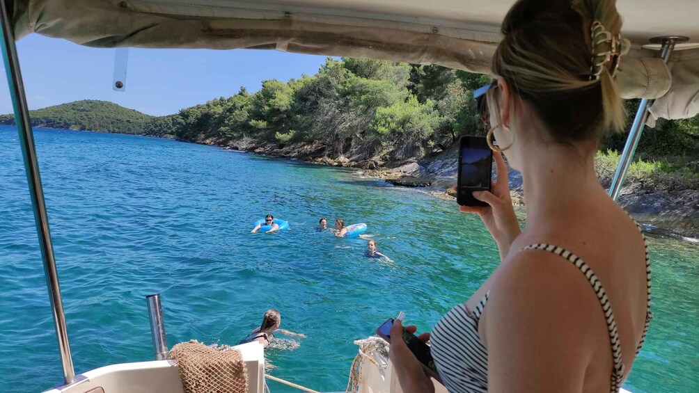 A person taking a photo of people swimming in a clear blue sea with a forested island in the background. 5