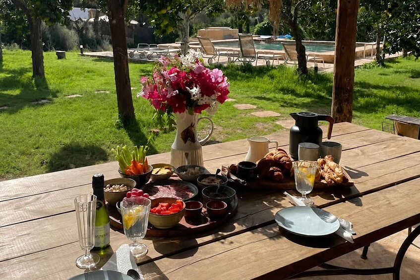 A picnic table with food, drinks, and a vase of flowers in a garden. 2