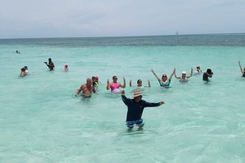 People swimming in clear turquoise water with a sailboat in the distance. 1