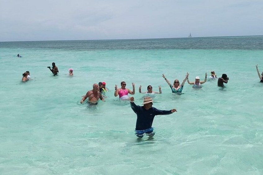People swimming in clear turquoise water with a sailboat in the distance. 4