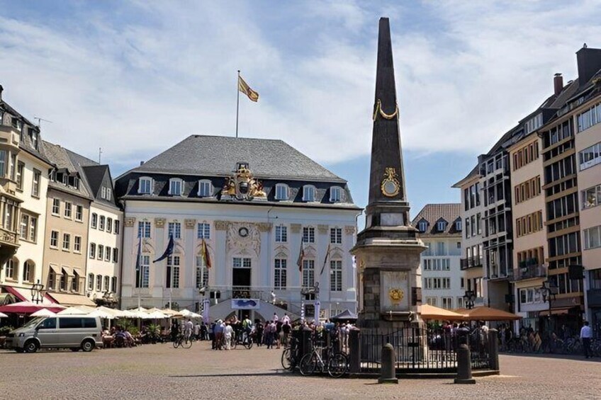 A public square with a monument, historic buildings, and a flag. 1
