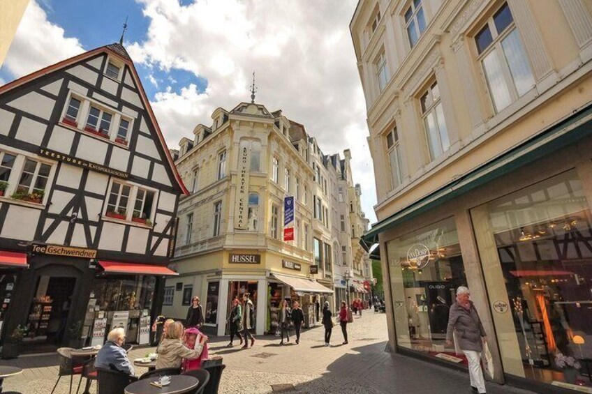 A European street with traditional half-timbered buildings, a HUSSEL shop, and people walking. 3