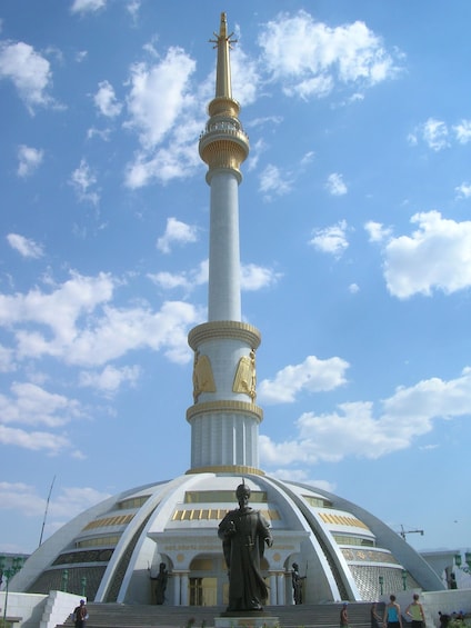 A tall white monument with a golden top, a statue at its base, and a dome-shaped building in the background. 3